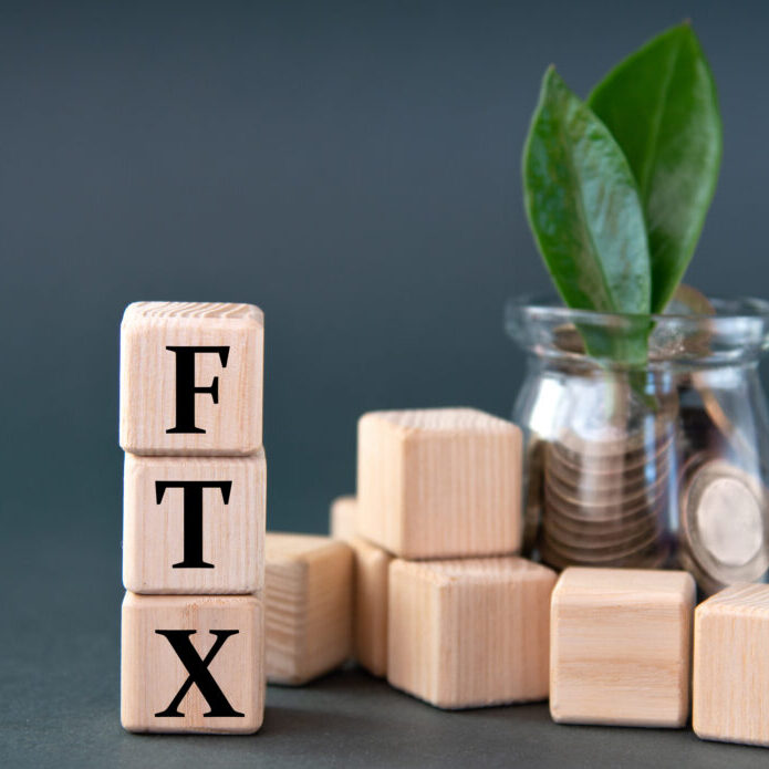 FTX - acronym on wooden cubes on the background of a glass jar with coins and green leaves. Business concept