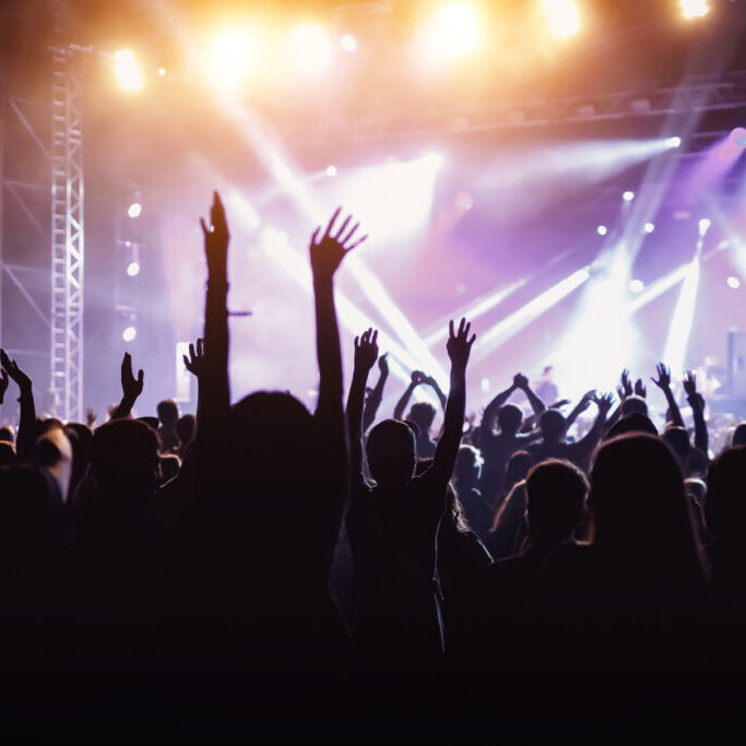 Rock concert, cheering crowd in front of bright colorful stage lights, Hands up with pleasure from the show