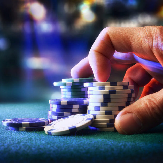 Hand betting game chips on felt mat with game room in the background. Front view.