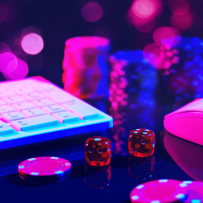 Close-up shot of red dice on a pink surface with a computer keyboard and mouse in the background.