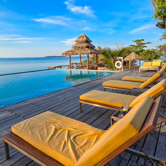 Lounging by the infinity pool on Koh Munnork Island offers breathtaking views of the turquoise ocean under a clear blue sky. This tranquil paradise is perfect for relaxation and escape in Thailand.
