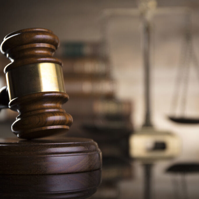 Statue of justice, gavel, scale and books on glass table.