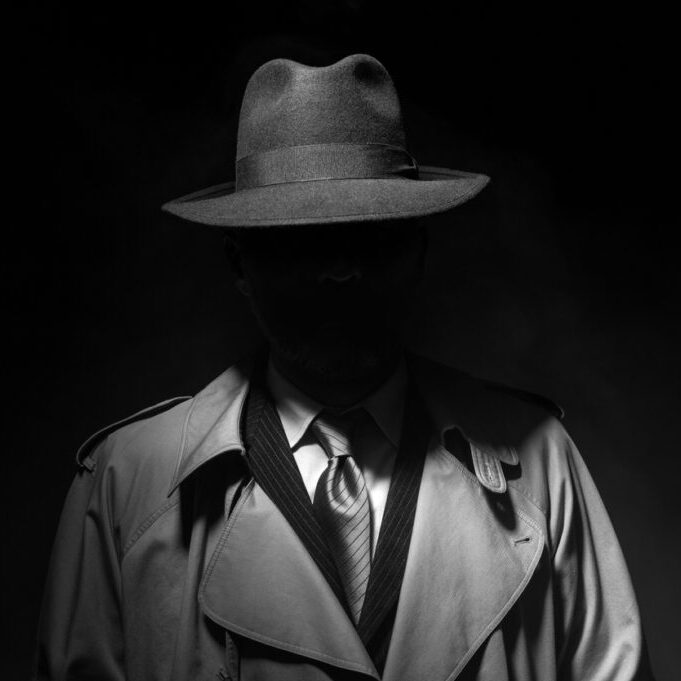 Man posing in the dark with a fedora hat and a trench coat, 1950s noir film style character