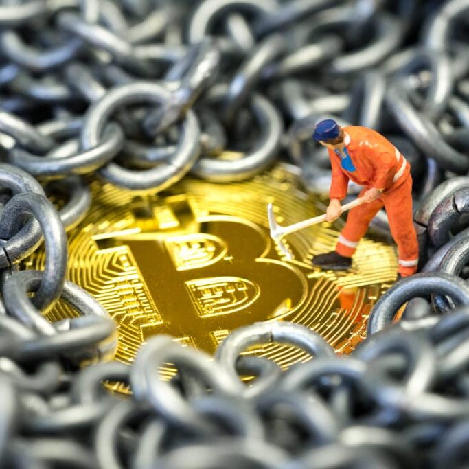 Bitcoin mining by miniature worker, small mini figure holding mattock digging on shiny golden physical Bitcoin Crpto currency coin surround by metal chains or blockchain concept.