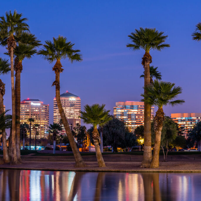 The lights of downtown Phoenix office buildings are reflected in the waters of the Encanto Park lagoon.